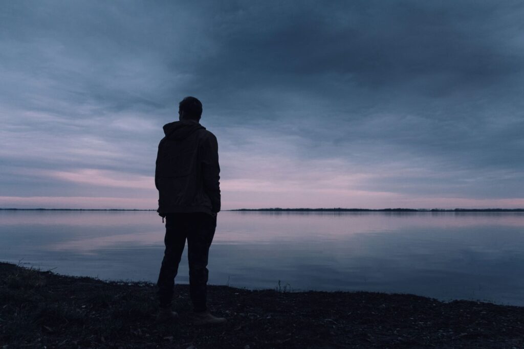 Zdjęcie samotnego mężczyzny stojącego przed zbiornikiem wodnym w czasie wieczoru